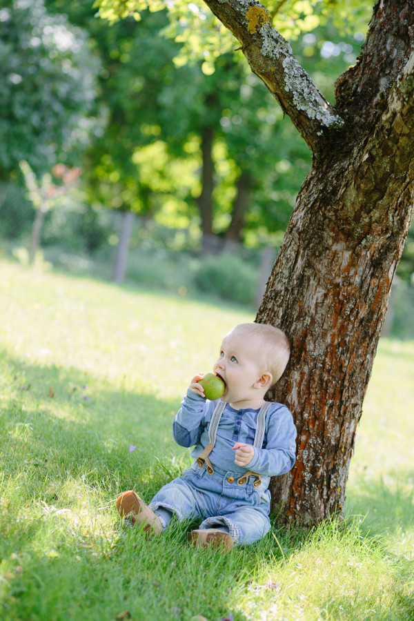 Kind sitzt an Baum gelehnt und isst Apfel