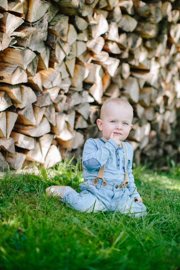 Kind sitzt im Gras vor Holz