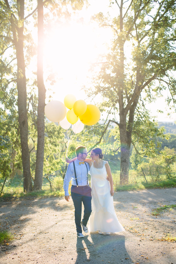 Brautpaar läuft Arm in Arm mit Luftballons, Sonne im Hintergrund